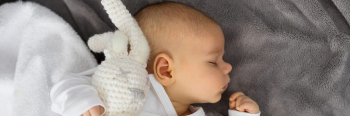 Bebé abrazado a conejito de crocket sobre manta gris. Bebé dormidito en cuna.